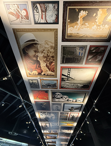 Long ceiling gallery of framed photographs and artwork above the dining room