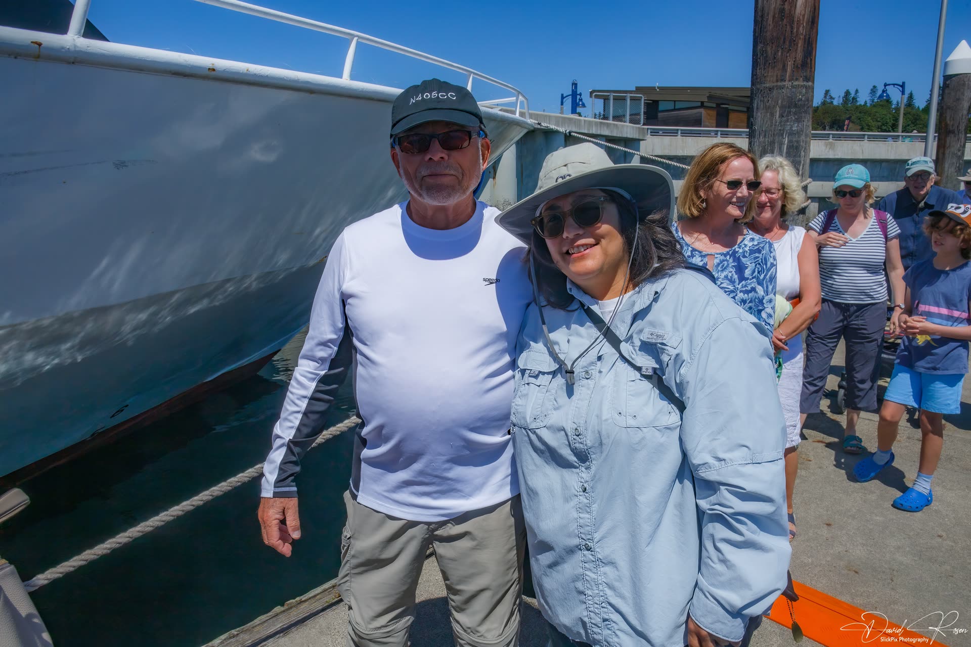 Two guests pose beside the vessel with other passengers behind them.